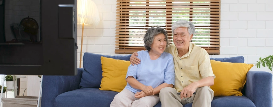 Life Assure Senior Couple Sitting On Couch Watching TV Hero